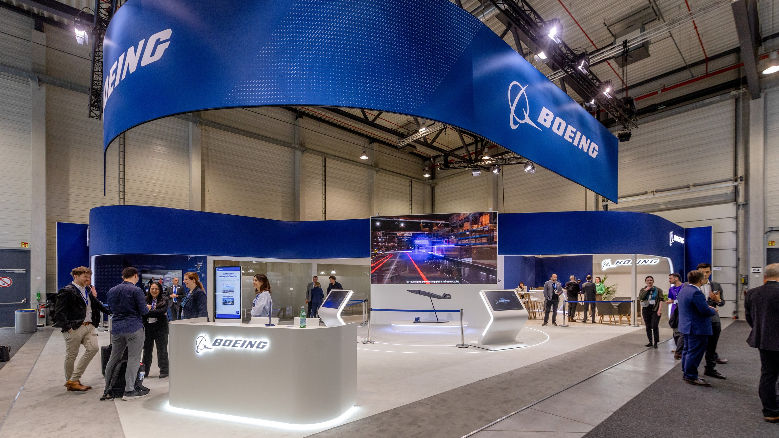 Wide-angle view of the Boeing stand in Hall C with a large blue overhead banner and an illuminated reception counter.