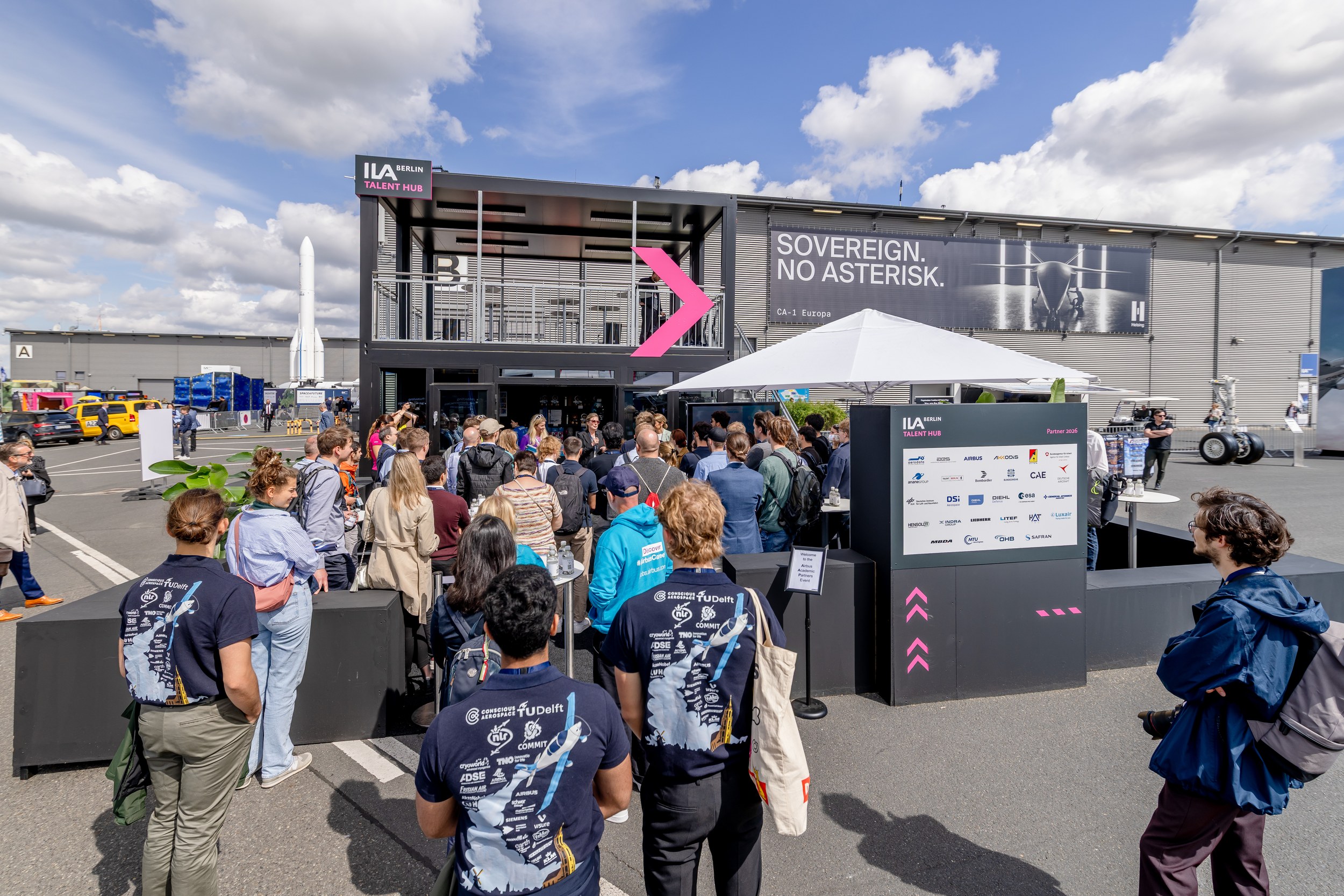 A wide outdoor view shows the ILA Berlin Talent Hub with a dense visitor group before the entrance and a large partner b