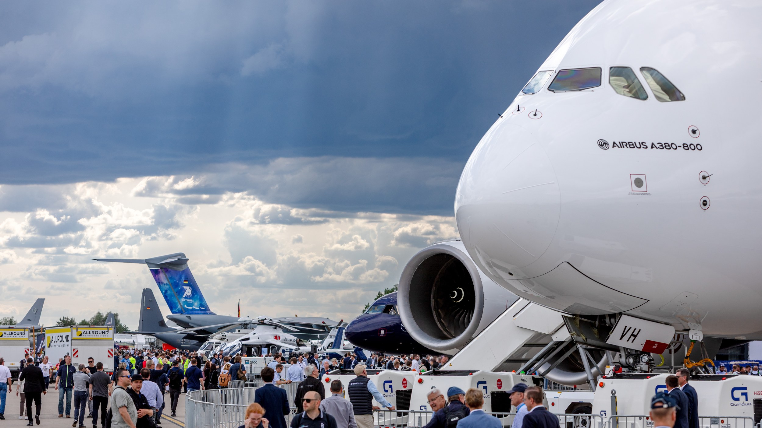 The nose of an Airbus A380-800 dominates the static display at right, with trade visitors moving along barriers and …