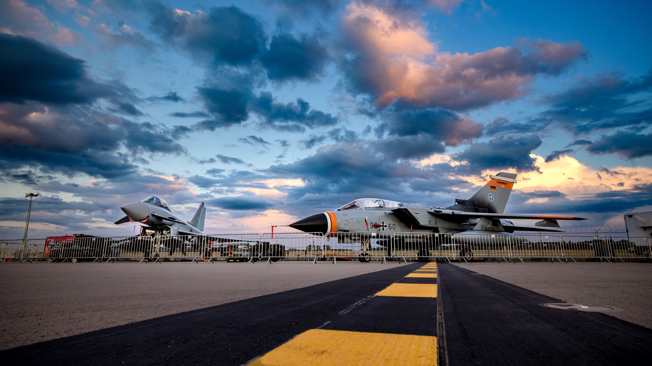 A Eurofighter Typhoon on the left and a Panavia Tornado carrying the serial 98+60 on the right stand behind metal barrie
