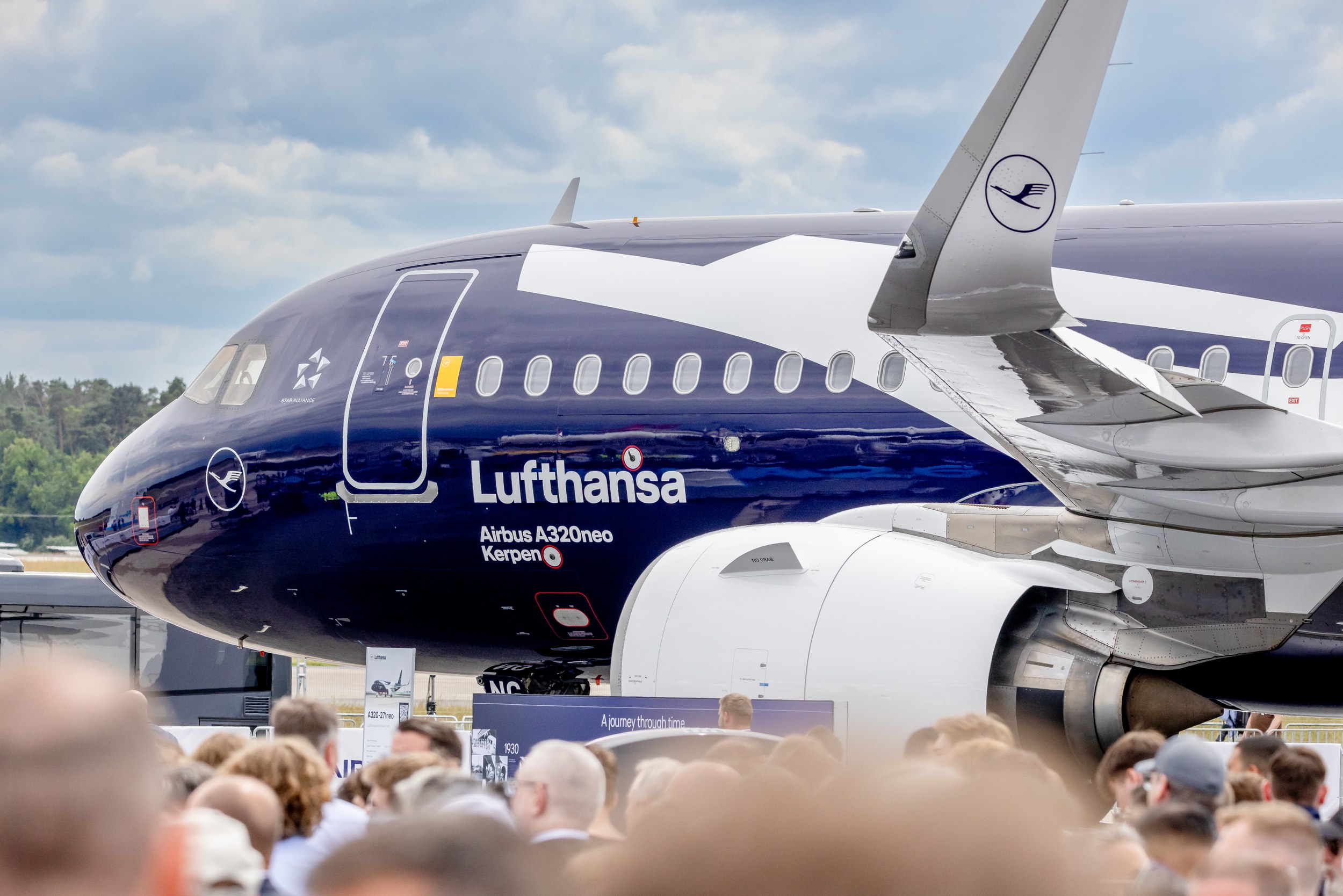 The dark-blue Lufthansa Airbus A320neo named “Kerpen” stands in the static display behind a dense crowd of trade visitor