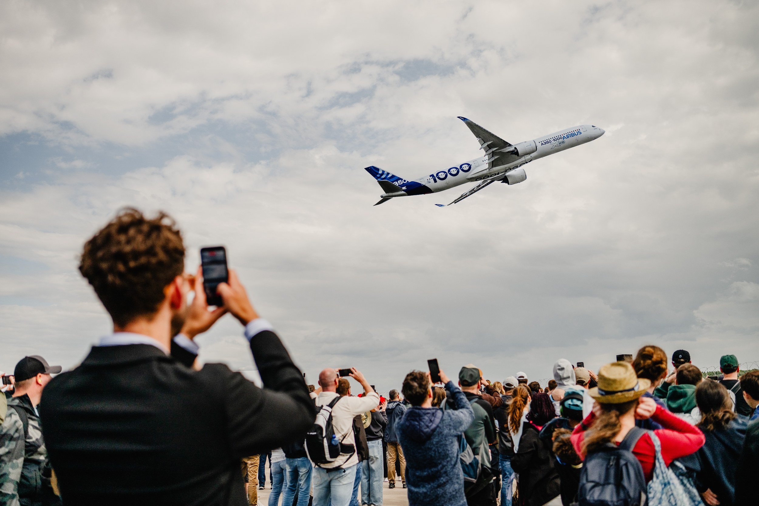 A large crowd points smartphones and cameras at an Airbus A350-1000 during the flying display.