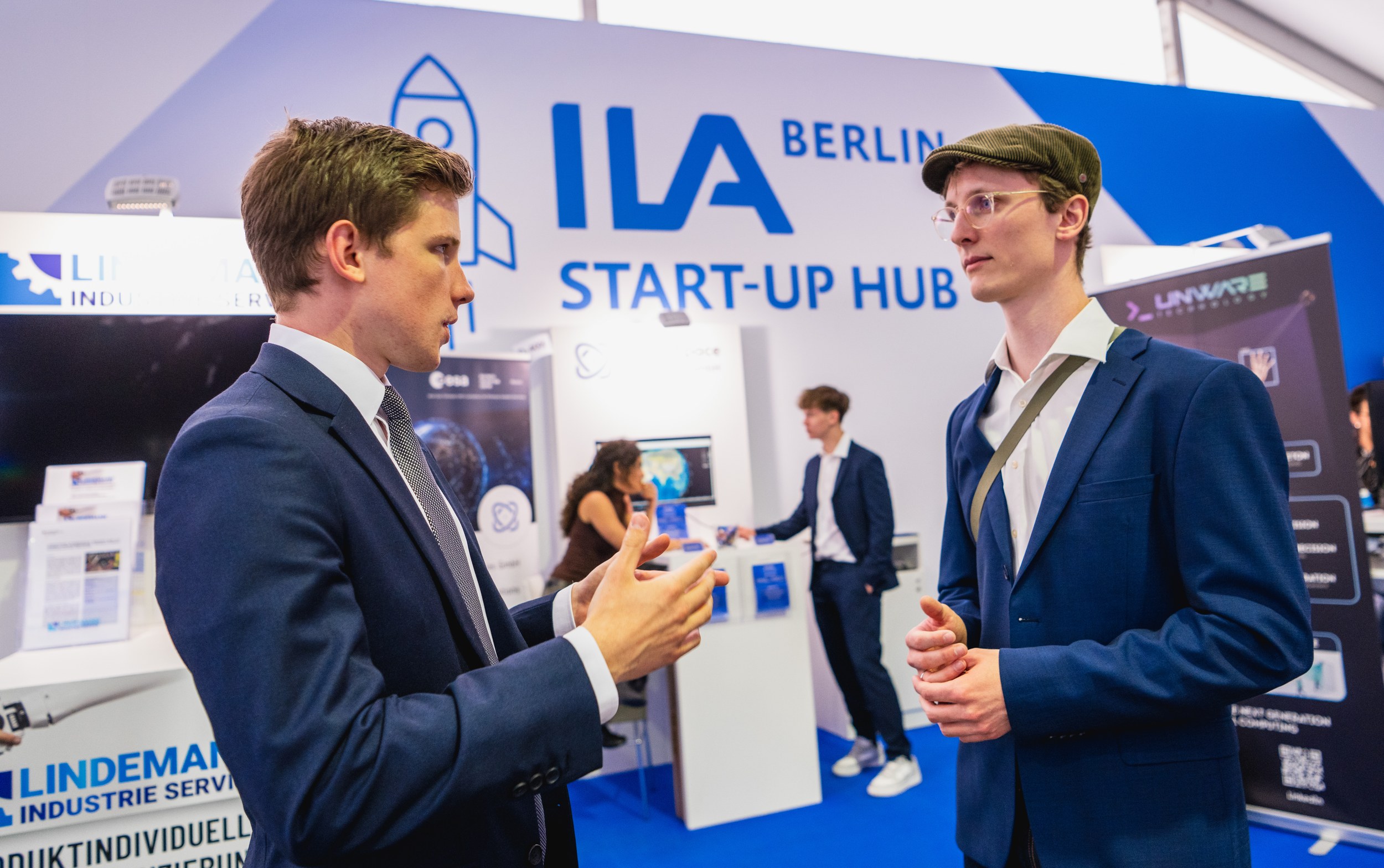 Two men face each other in the foreground of the ILA Start-up Hub and hold a focused conversation.