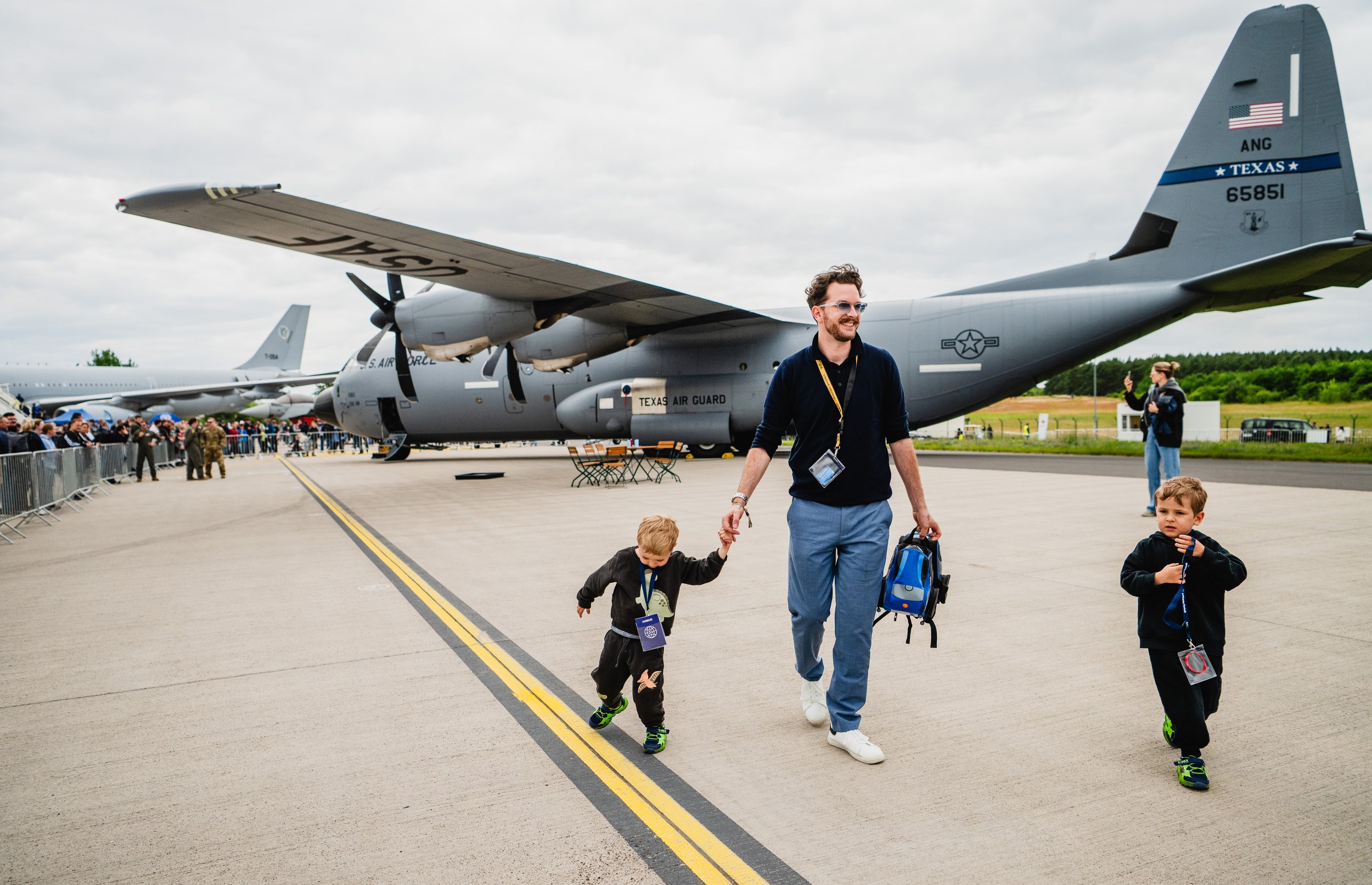 A father walks with two young children across the apron in front of a grey Lockheed Martin C-130 Hercules operated by …