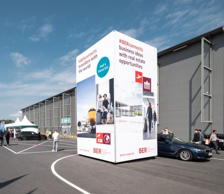 Free-standing advertising tower with large-scale brand advertising on an ILA site axis.